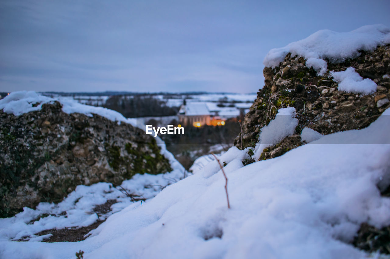 Snow covered rocks against sky - small church in background - early winter morning 