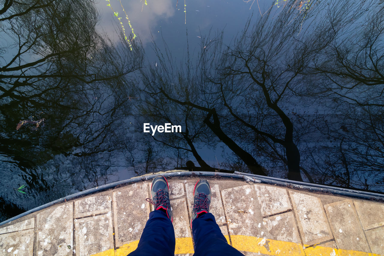 Low section of man standing by lake with trees reflecting