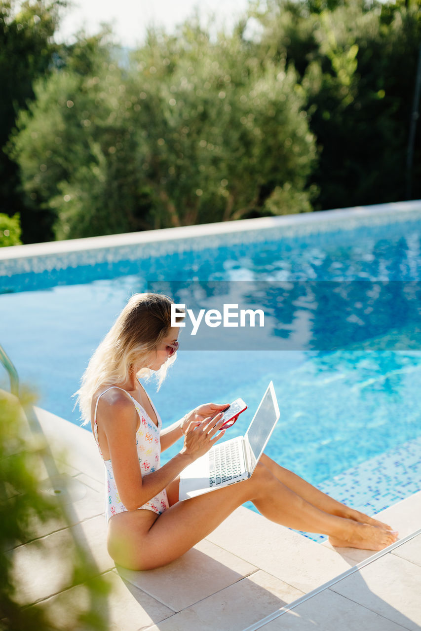 portrait of young woman using mobile phone while swimming pool