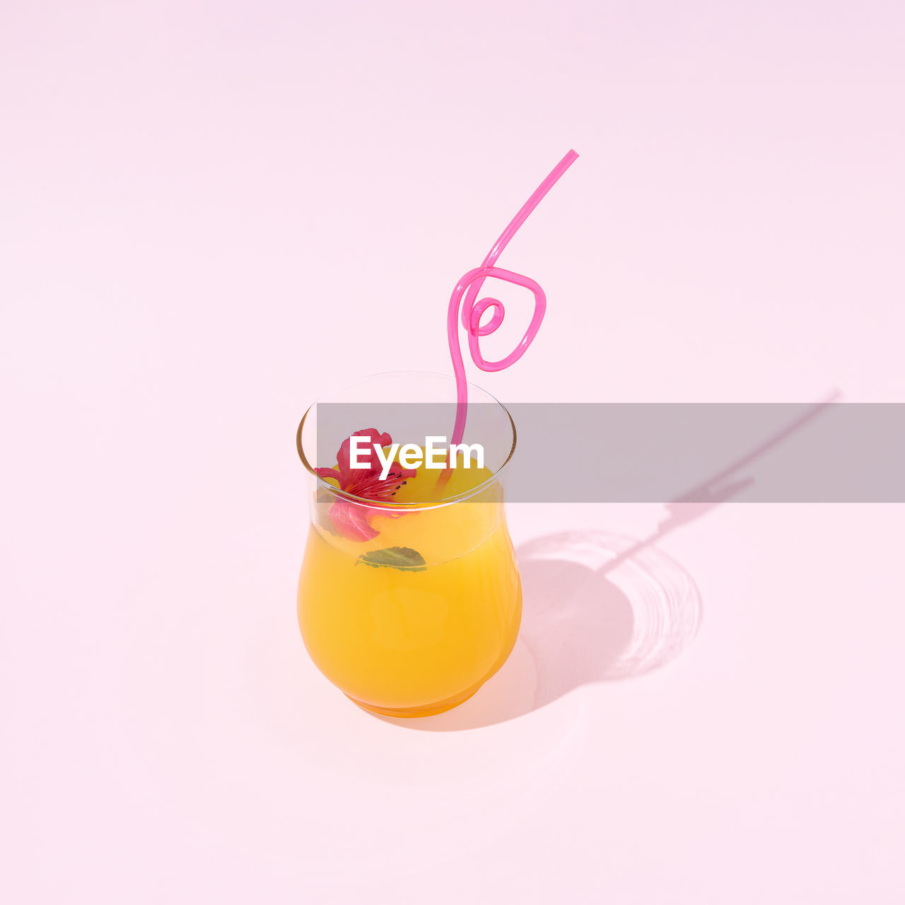 Orange juice in a glass with a plastic straw and a flower on a pink background. 