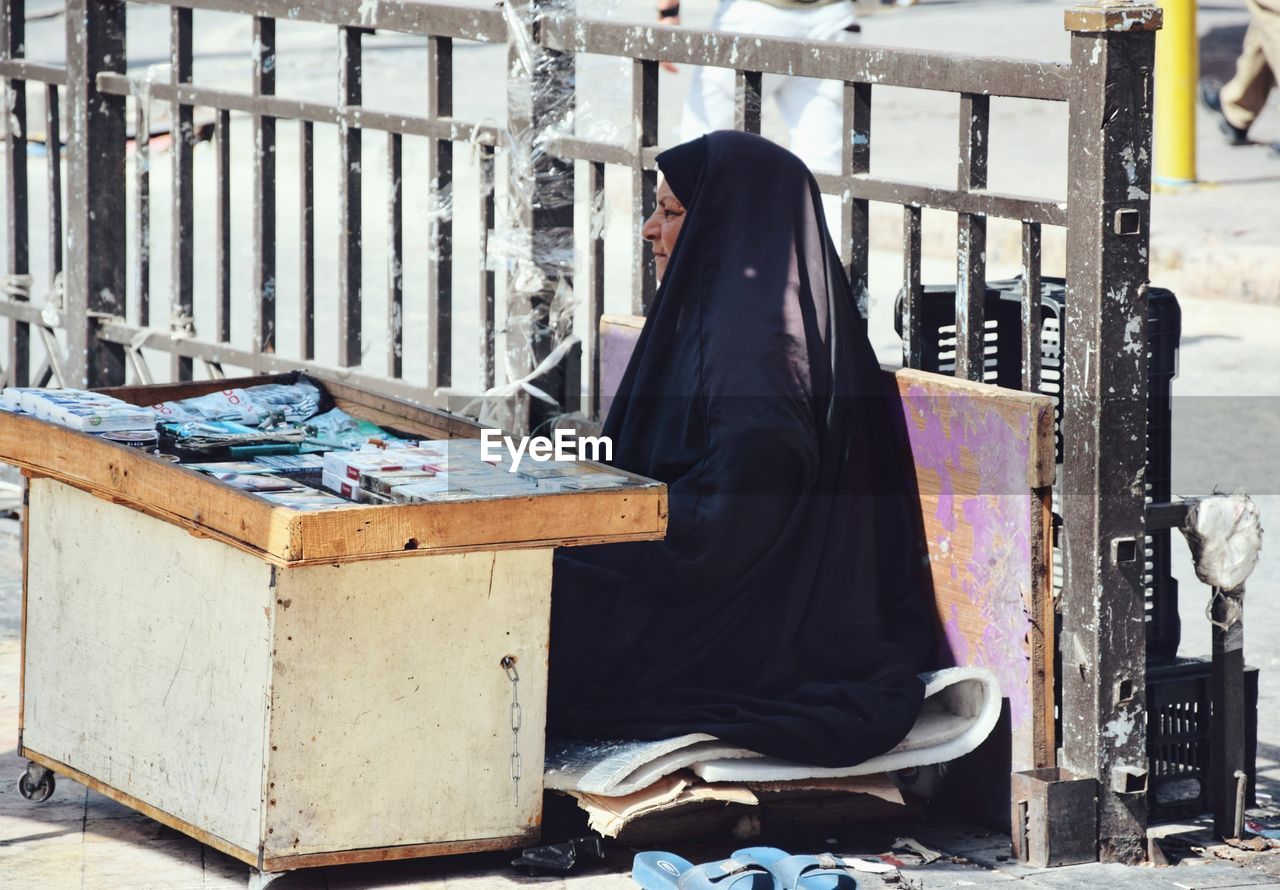 Side view of mature woman wearing hijab sitting at market stall