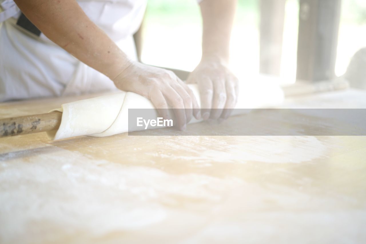 Midsection of chef rolling dough at commercial kitchen