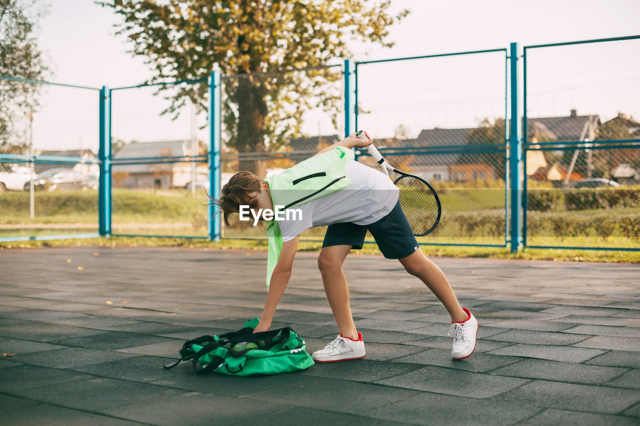 A young athlete takes a ball from a sports bag, holds a tennis racket in his hand
