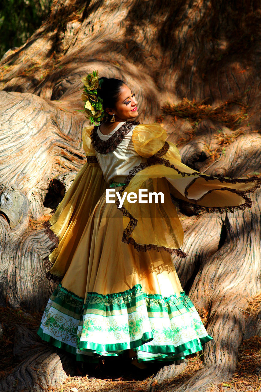 Young woman in traditional clothing dancing against large tree