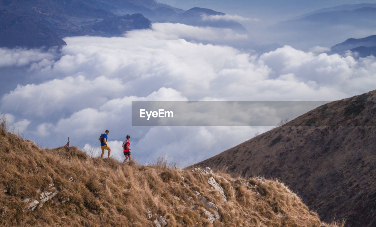 Side view of friends walking on mountain against cloudy sky