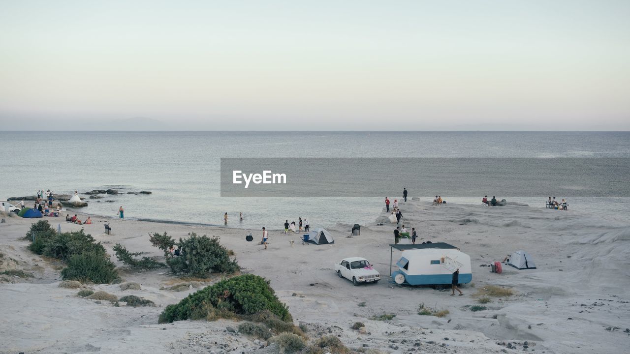 HIGH ANGLE VIEW OF CROWD ON BEACH AGAINST SKY