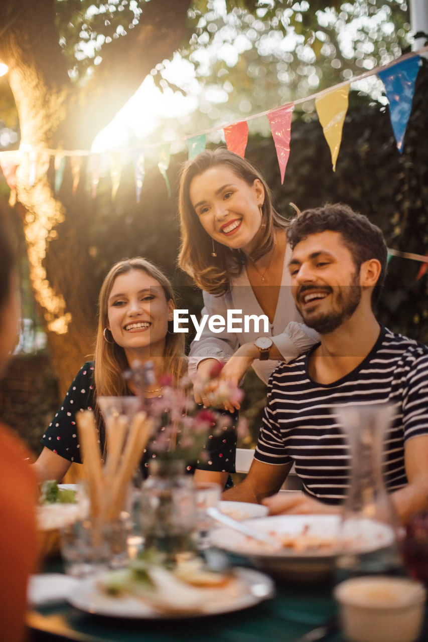 Happy young male and female friends at table during dinner party in backyard