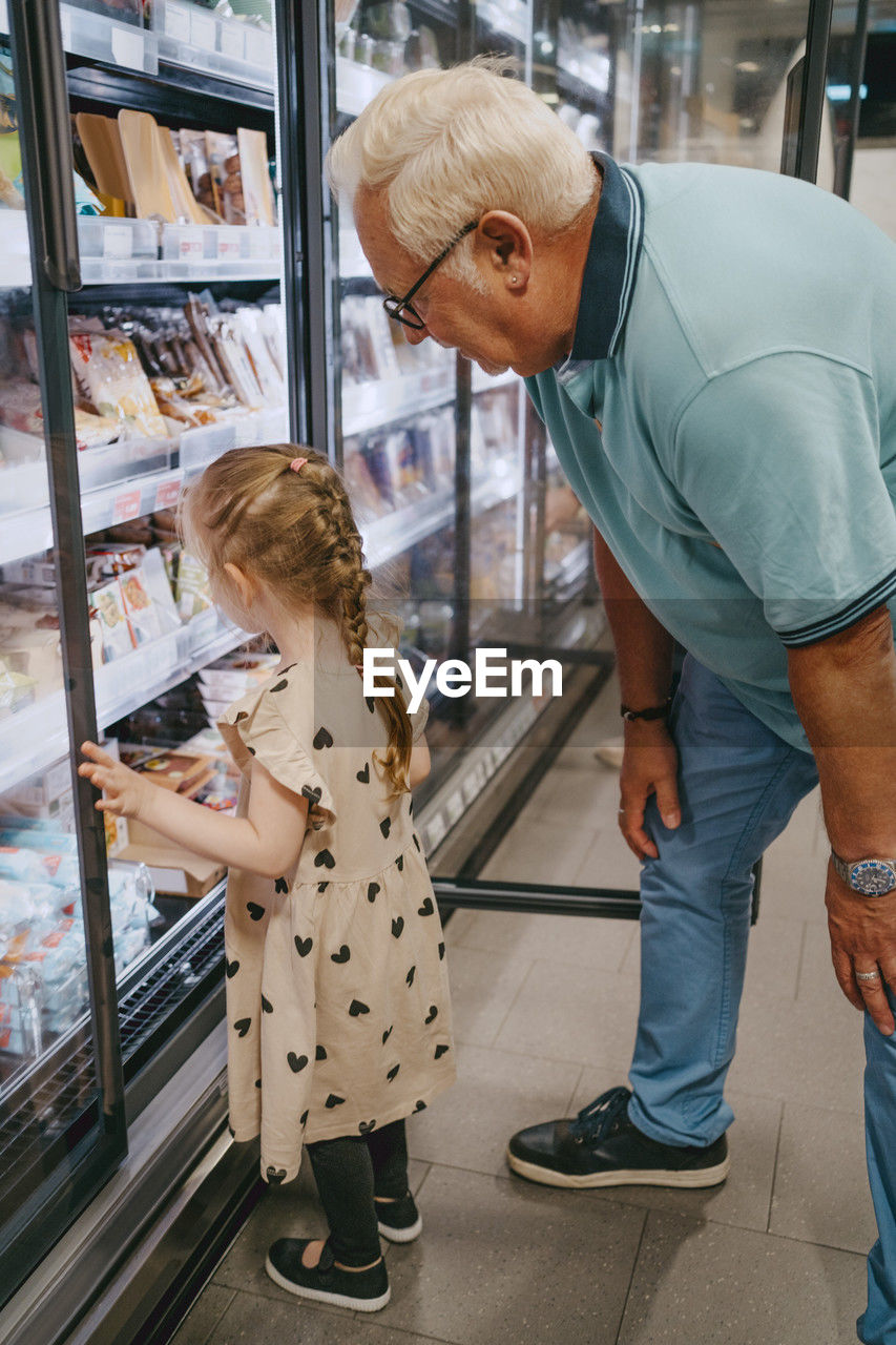 Girl buying frozen foods while doing shopping with grandfather at grocery store