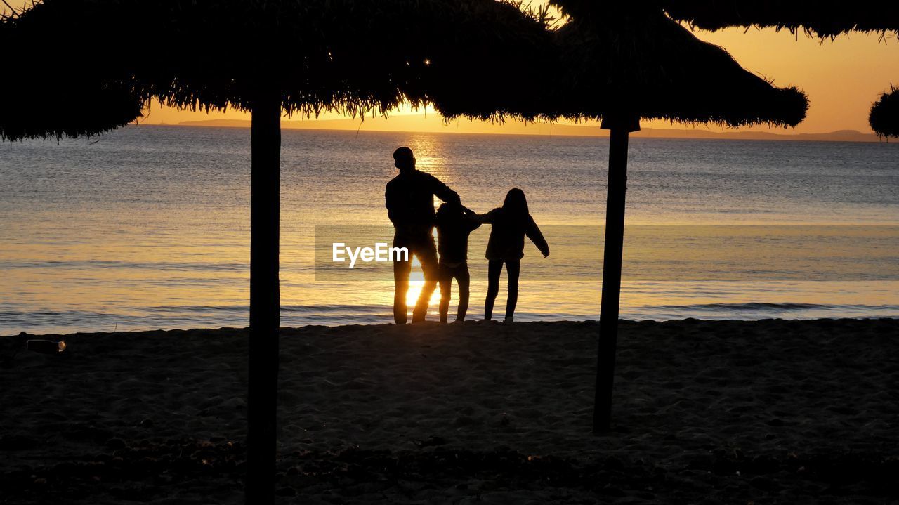 Silhouette men wirh kids on beach against sky during sunset