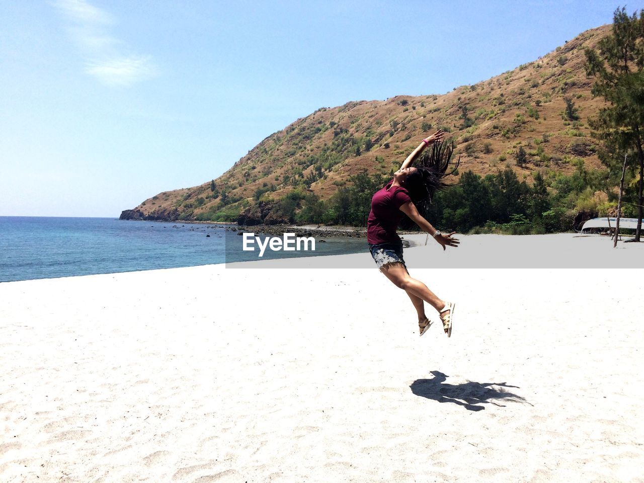 Woman jumping on sand by mountain at beach
