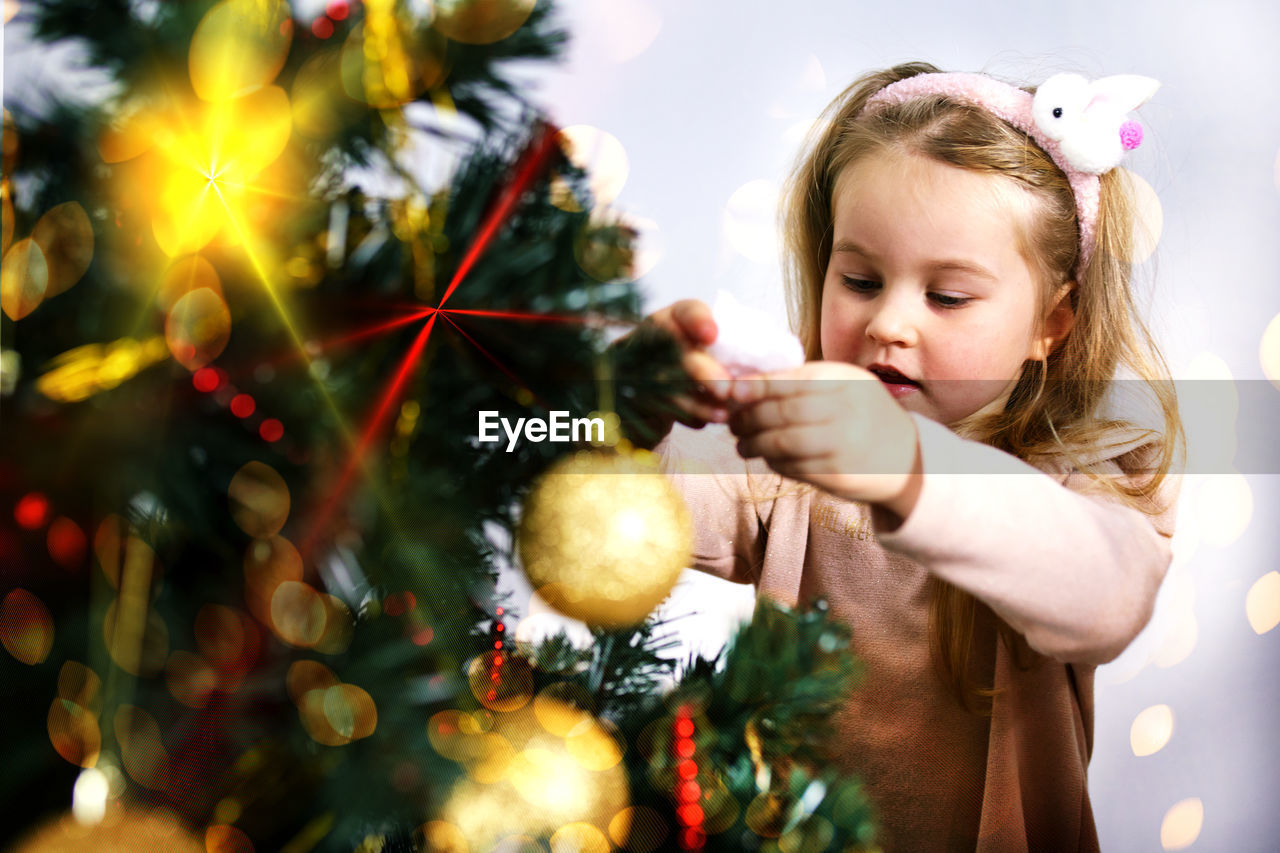 A small girl with white hair stands at the elegant christmas tree