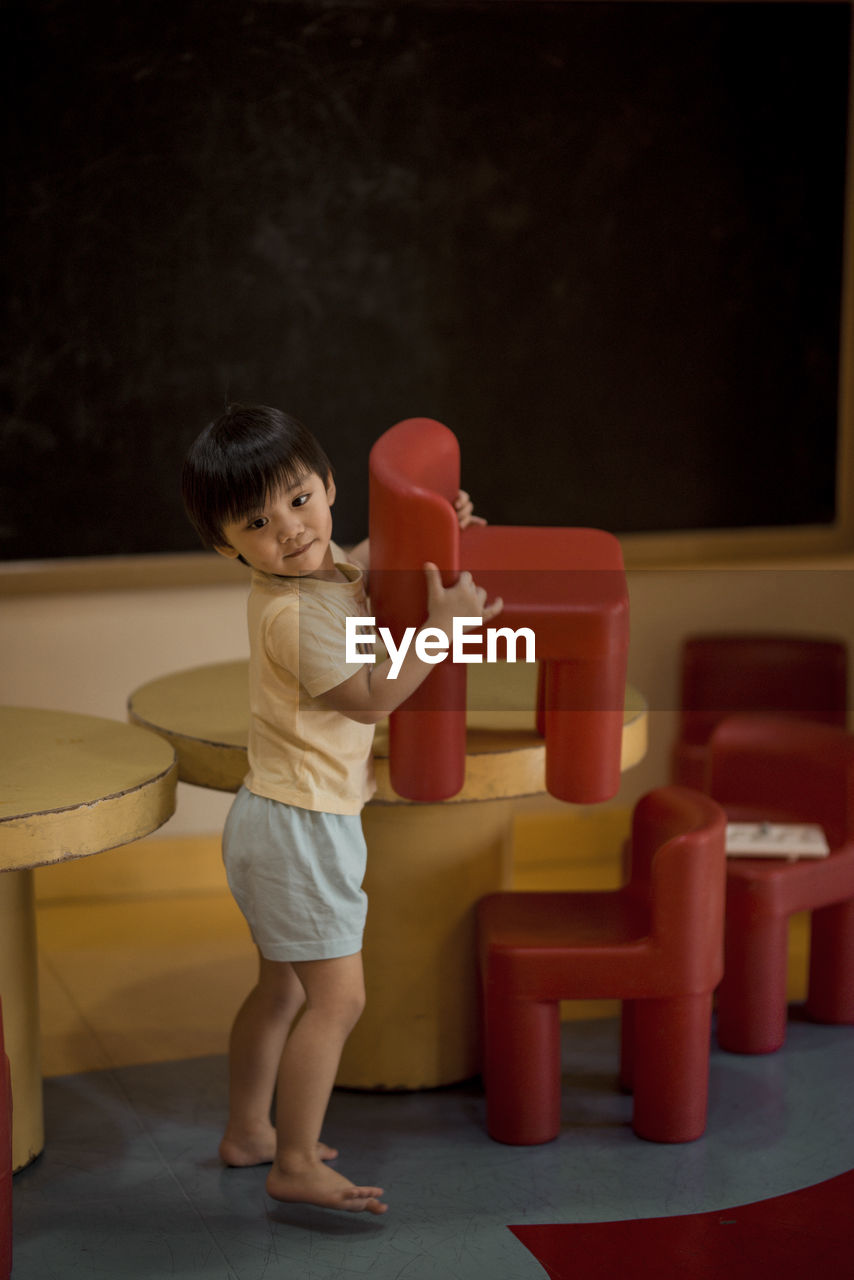 Full length of cute boy playing with chairs