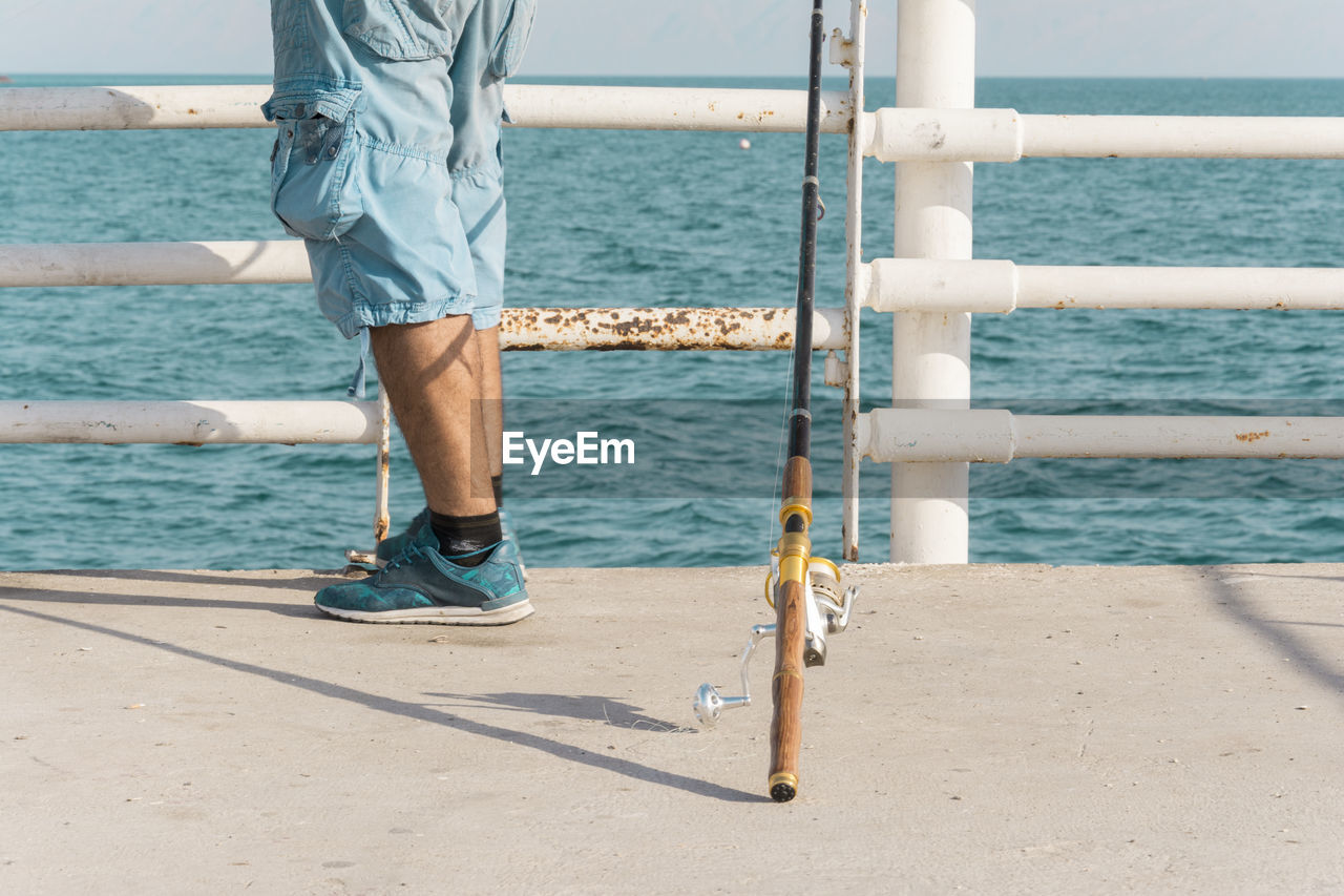 Low section of man standing by railing at beach