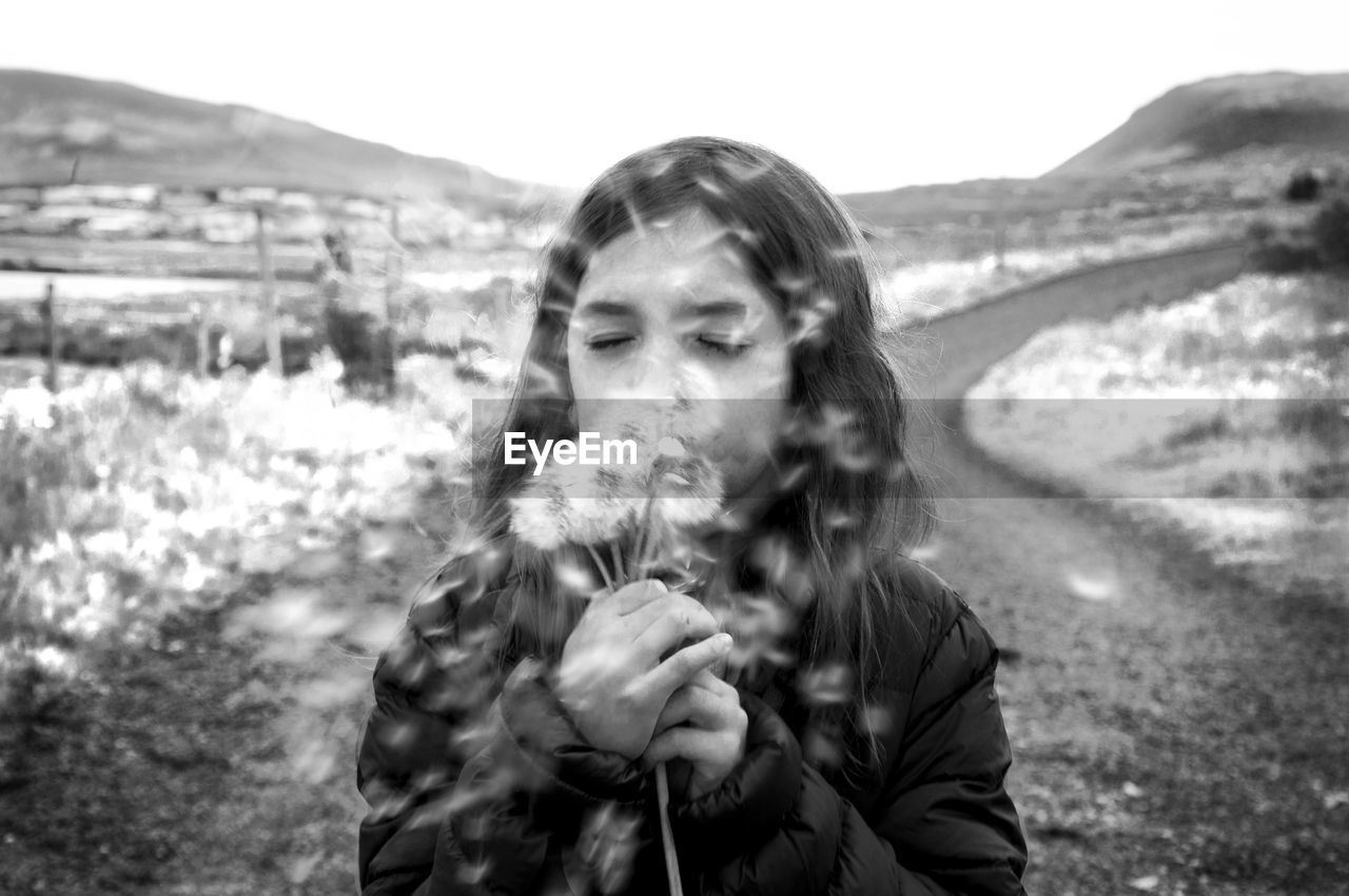 Cute girl with eyes closed blowing dandelions on field