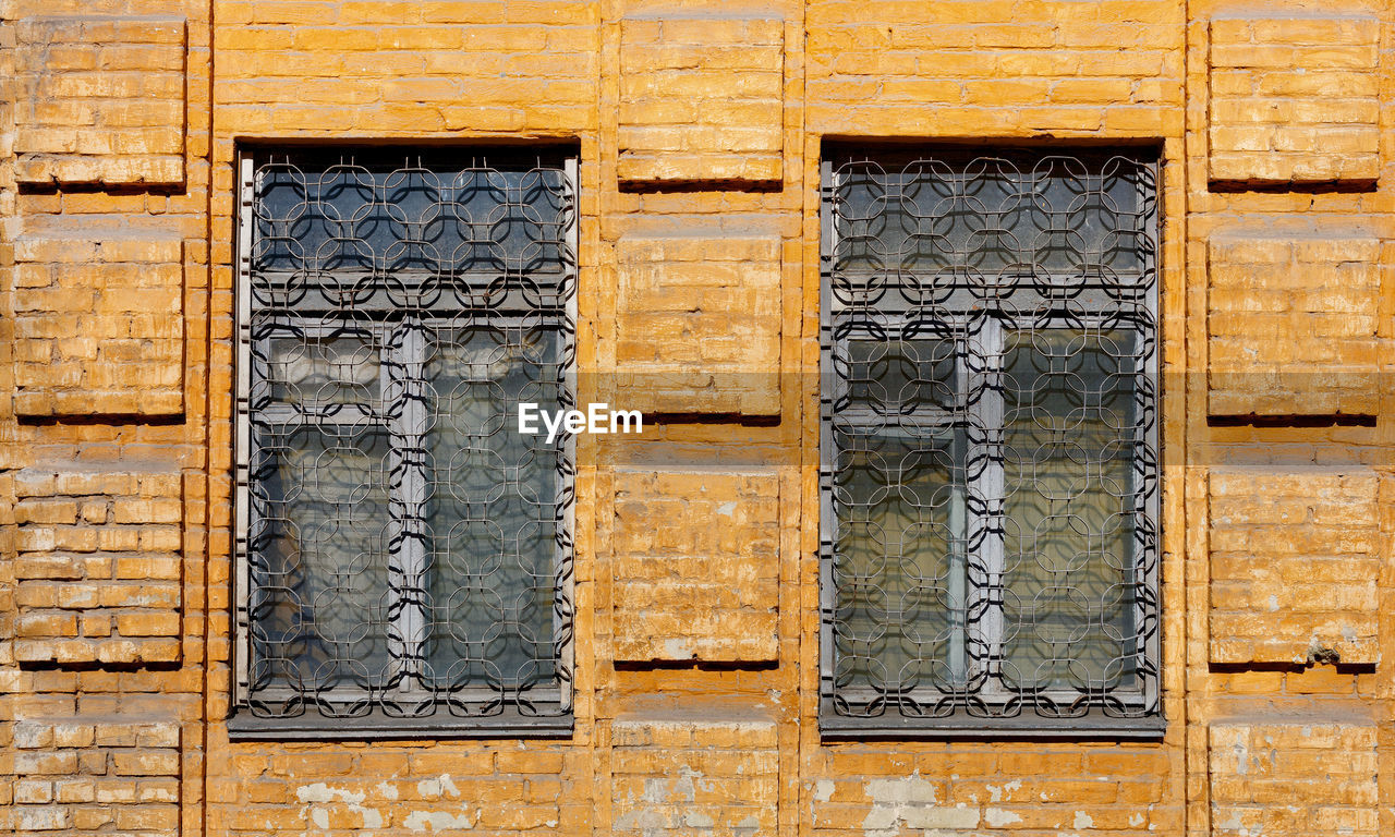 The old shabby brick facade of the house with metal figured bars on the windows, illuminated.