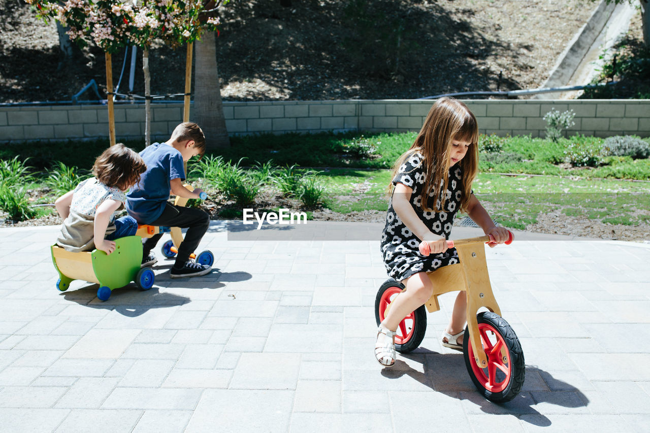 Three kids outside ride around on wooden bicycles