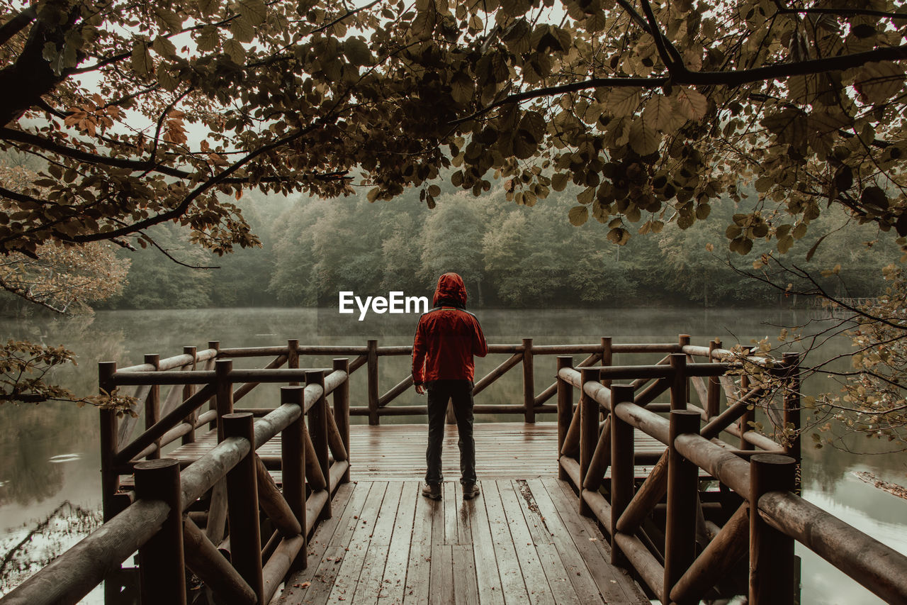 REAR VIEW OF WOMAN STANDING ON PIER AT FOOTBRIDGE
