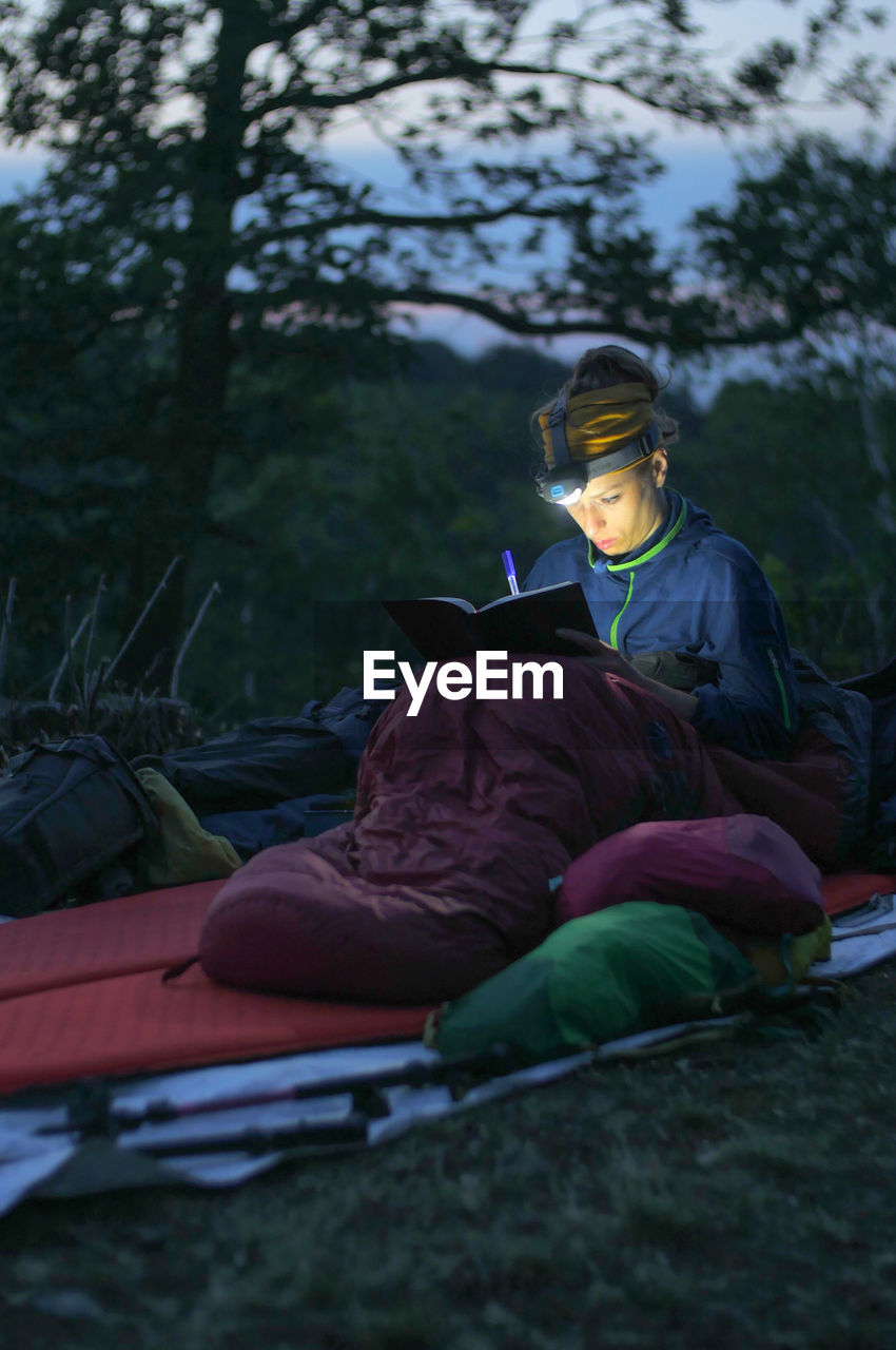 Woman writing in book while sitting on field