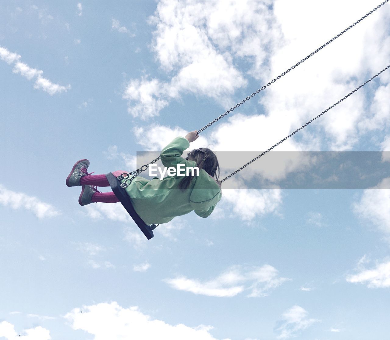Low angle view of girl swinging on swing against cloudy sky