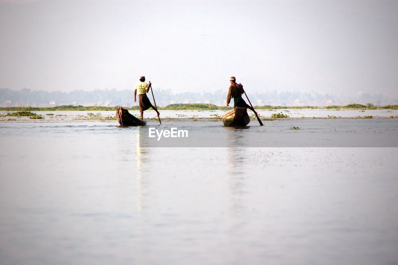 Fishermen in boat on sea against sky