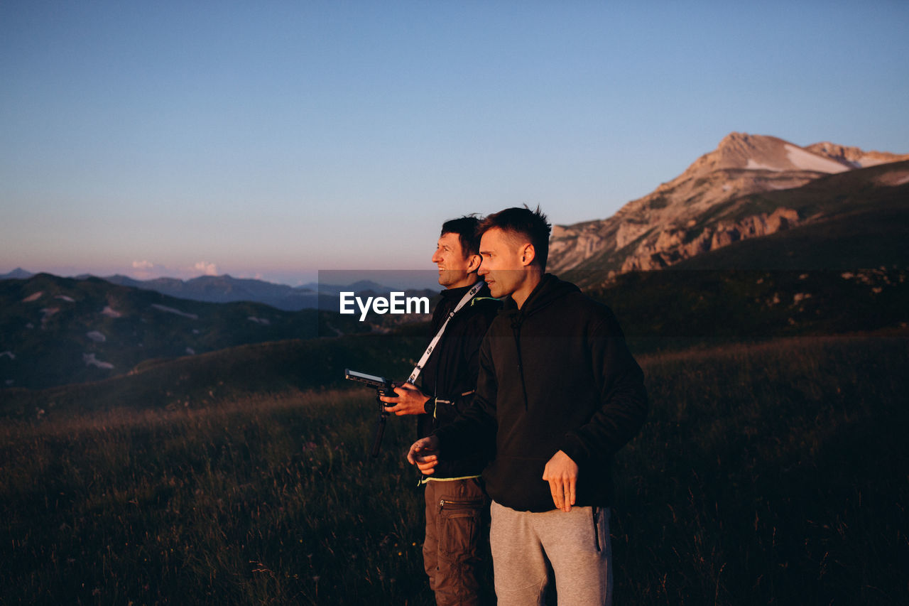 Man holding remote control of drone by friend against sky