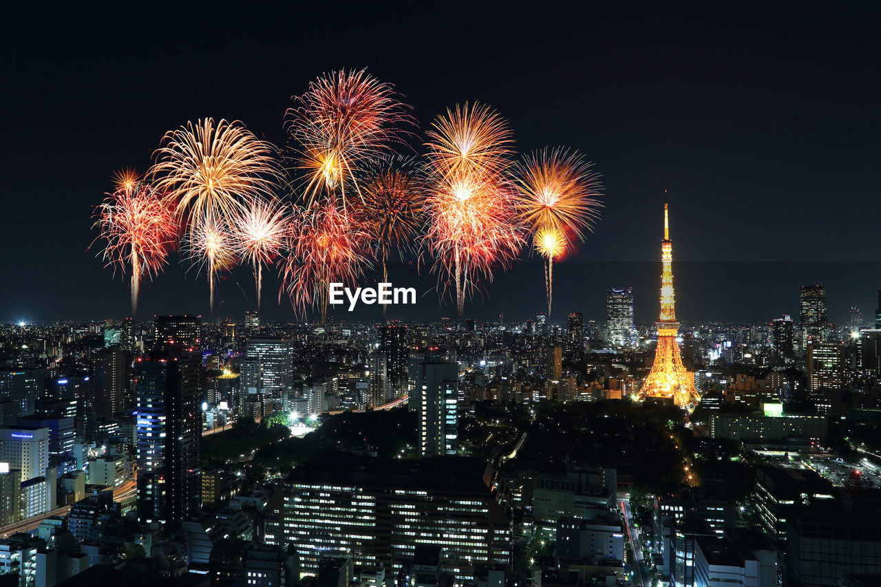 FIREWORK DISPLAY OVER ILLUMINATED BUILDINGS AGAINST SKY