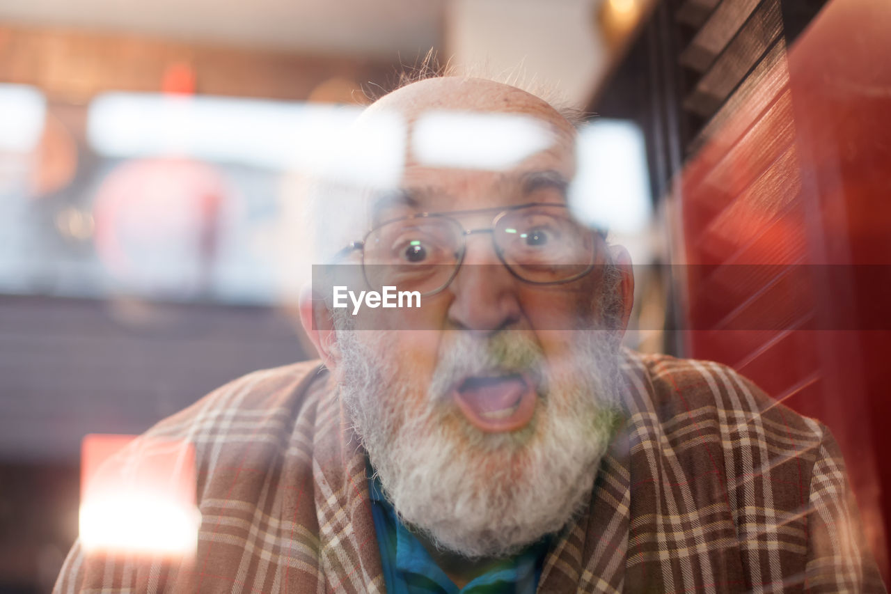 Portrait of shocked senior man seen through glass