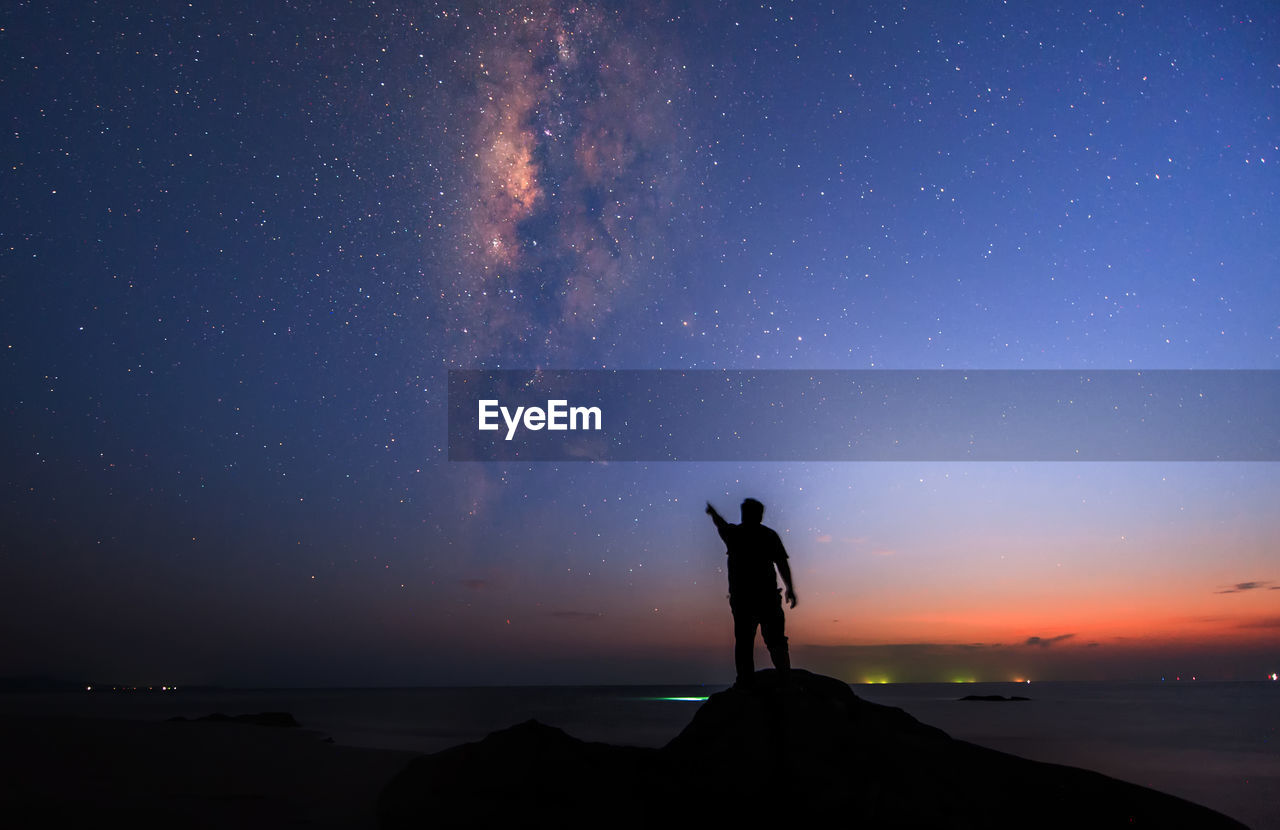 Silhouette man standing while pointing at galaxy in sky