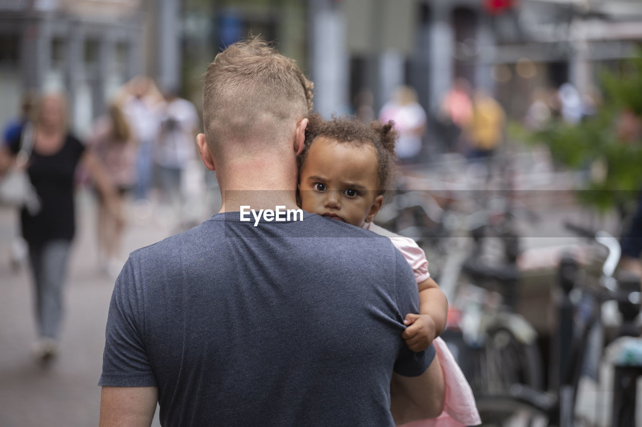 A young dad carrying his mixed race daughter in the city