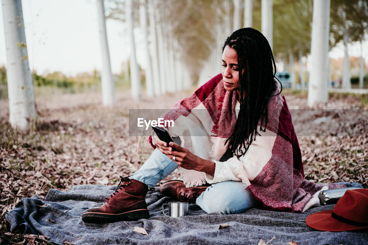 Full length of woman using smart phone while sitting amidst trees