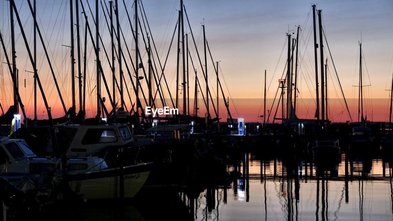 SAILBOATS MOORED IN HARBOR AT SUNSET