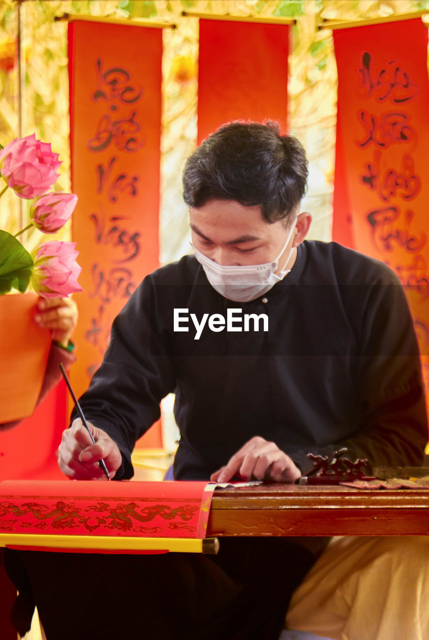 Man wearing mask writing on prayer flag