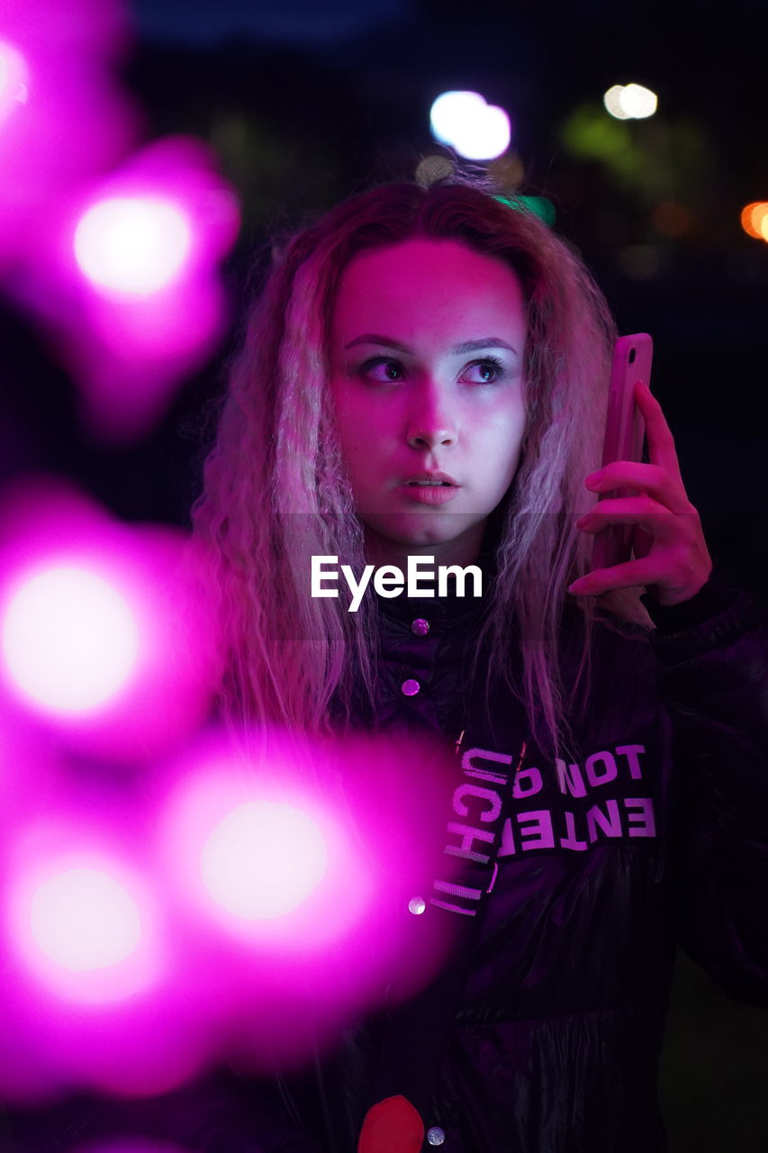 Medium close up in pink neon light with girl and phone