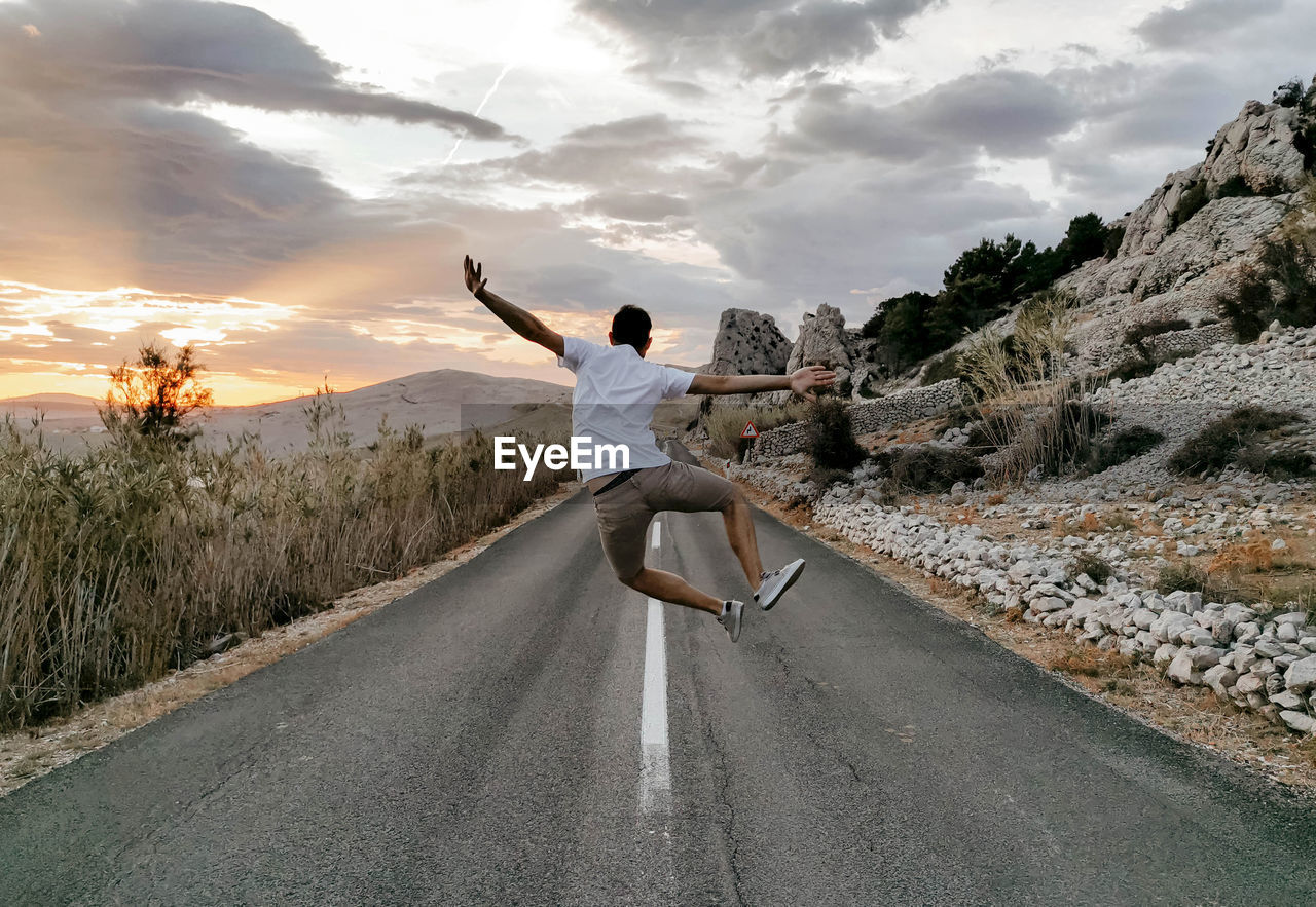 Rear view of man jumping in middle of open road. sumer, wanderlust, travel.