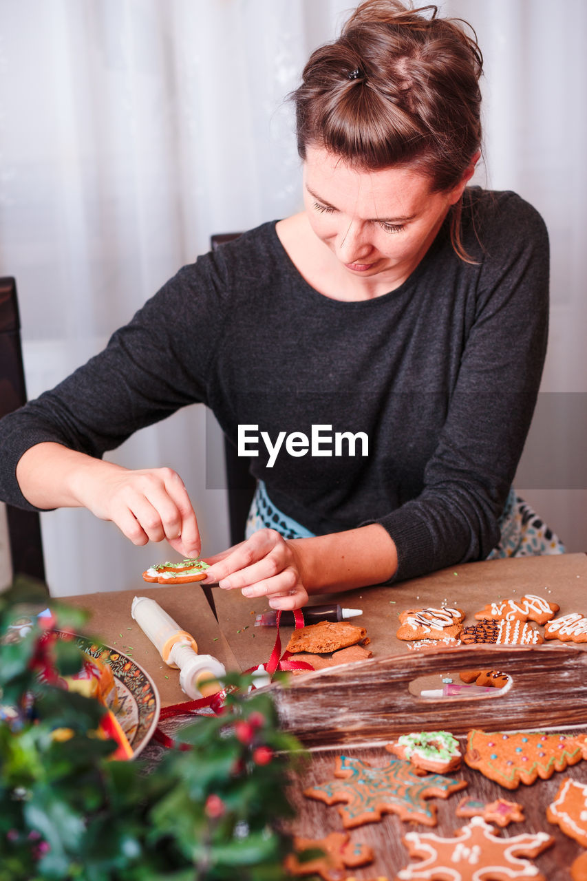 Woman decorating christmas gingerbread cookies at home