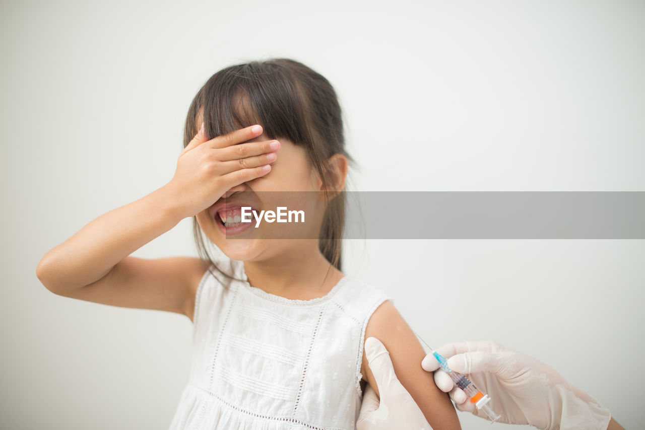 Cropped hand of doctor holding girl with syringe against white background