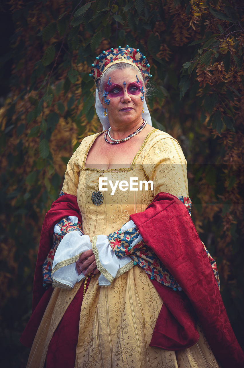 Thoughtful mature woman wearing period costume while standing against tree