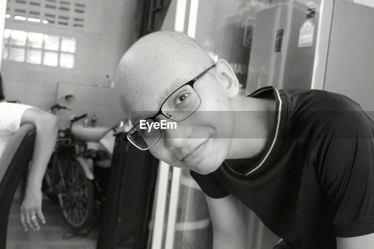 Portrait of smiling bald teenage boy wearing eyeglasses at home