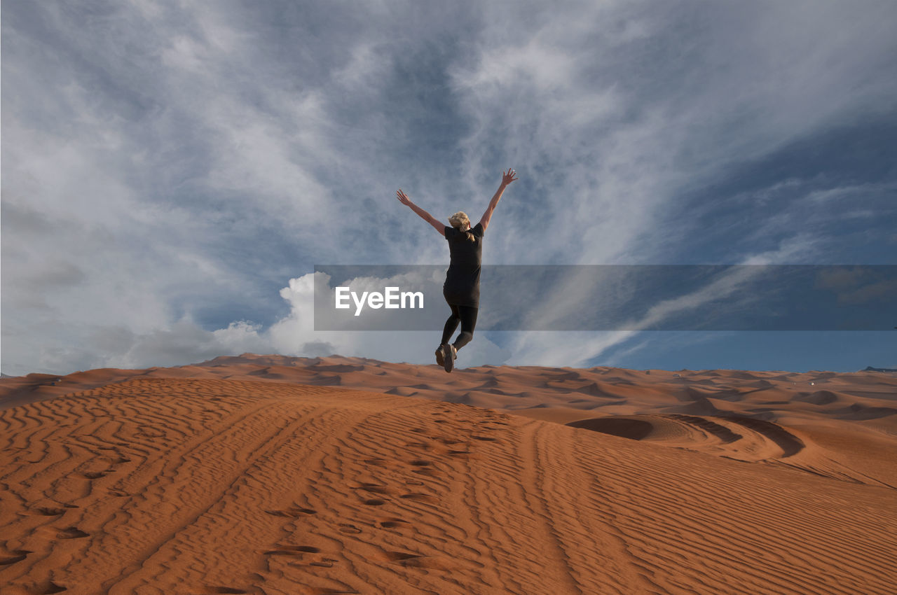 Rear view of person jumping on sand at desert