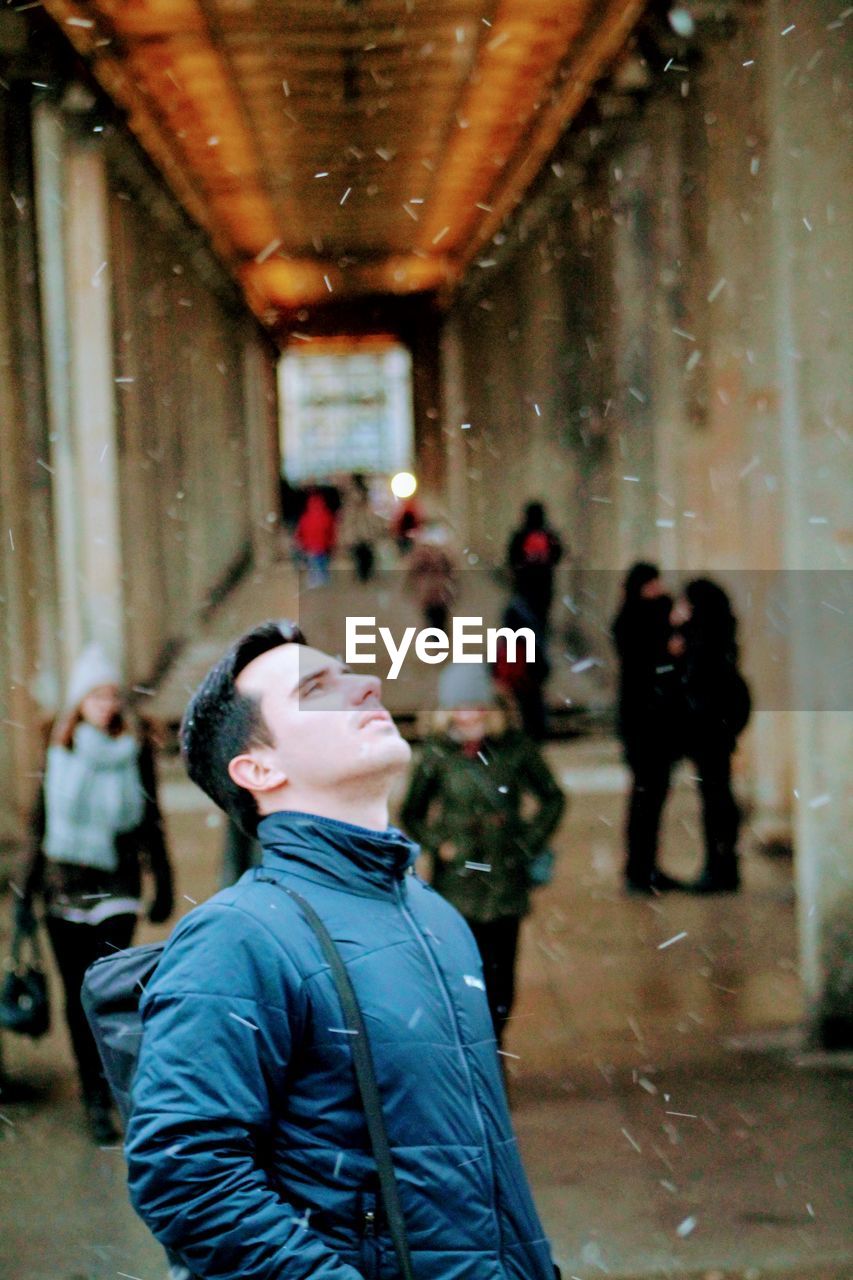 Handsome man looking up during snowfall in city