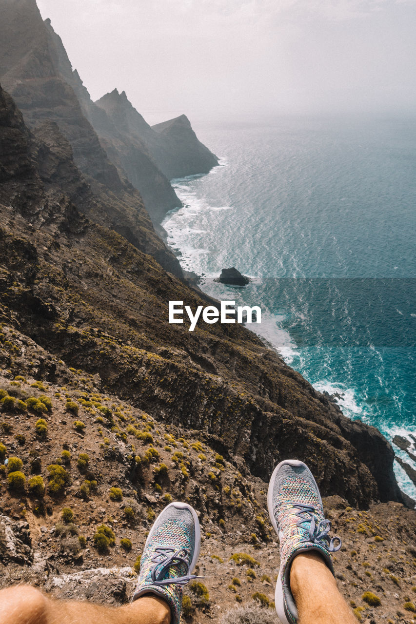 LOW SECTION OF MAN STANDING ON ROCK BY SEA