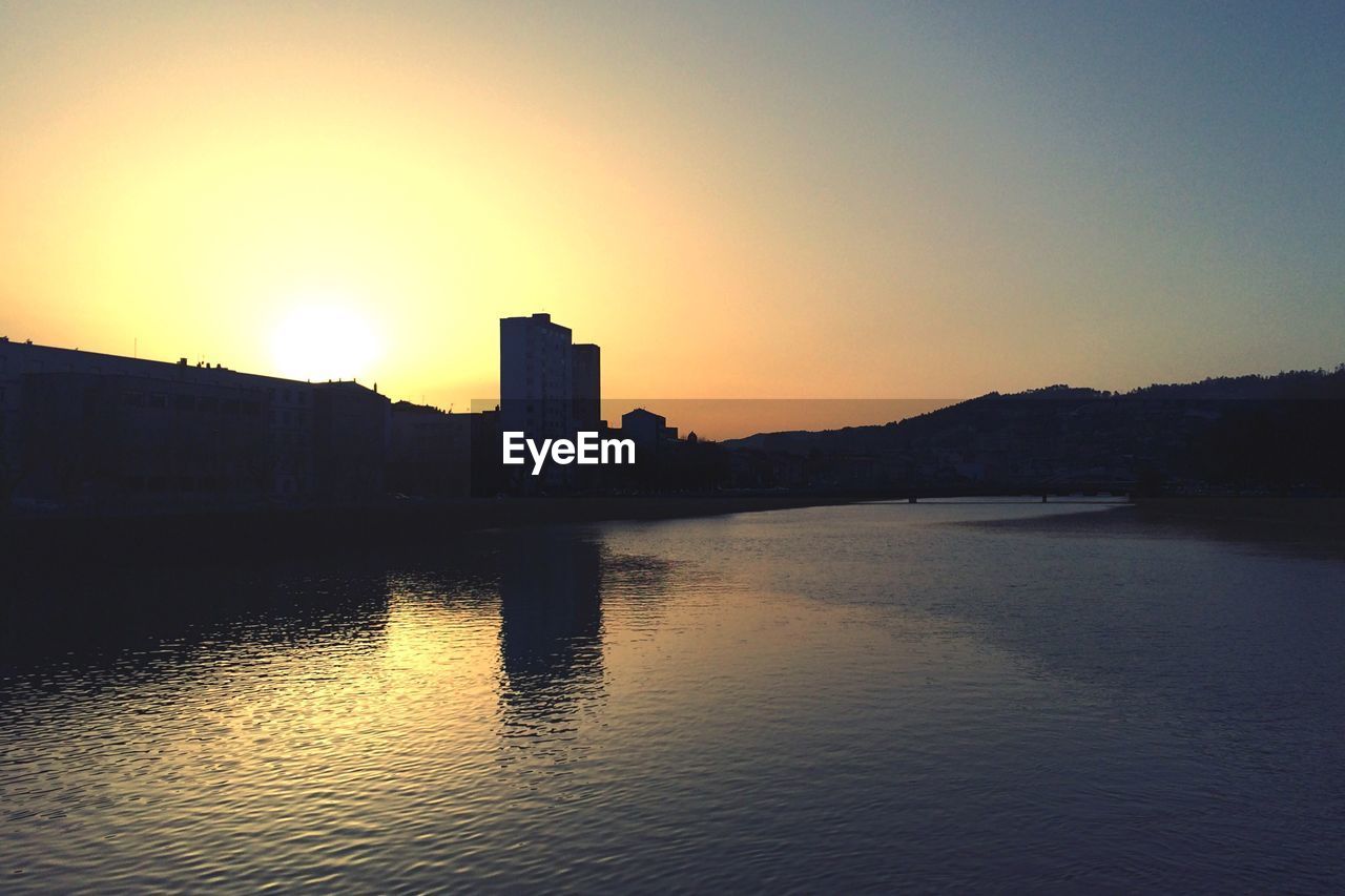 Scenic view of lake by buildings against sky during sunset