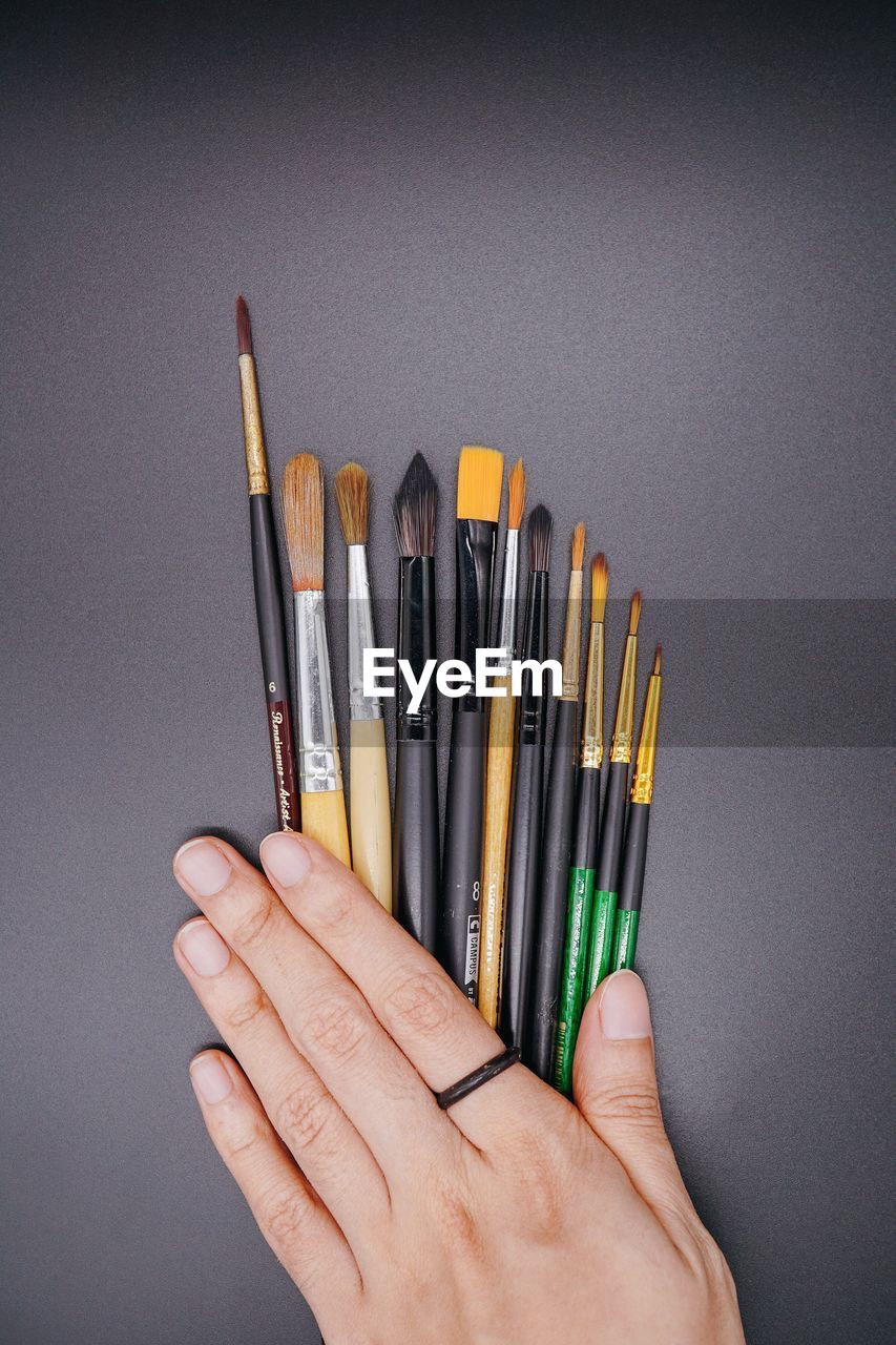CLOSE-UP OF HAND HOLDING COLORED PENCILS OVER WHITE BACKGROUND