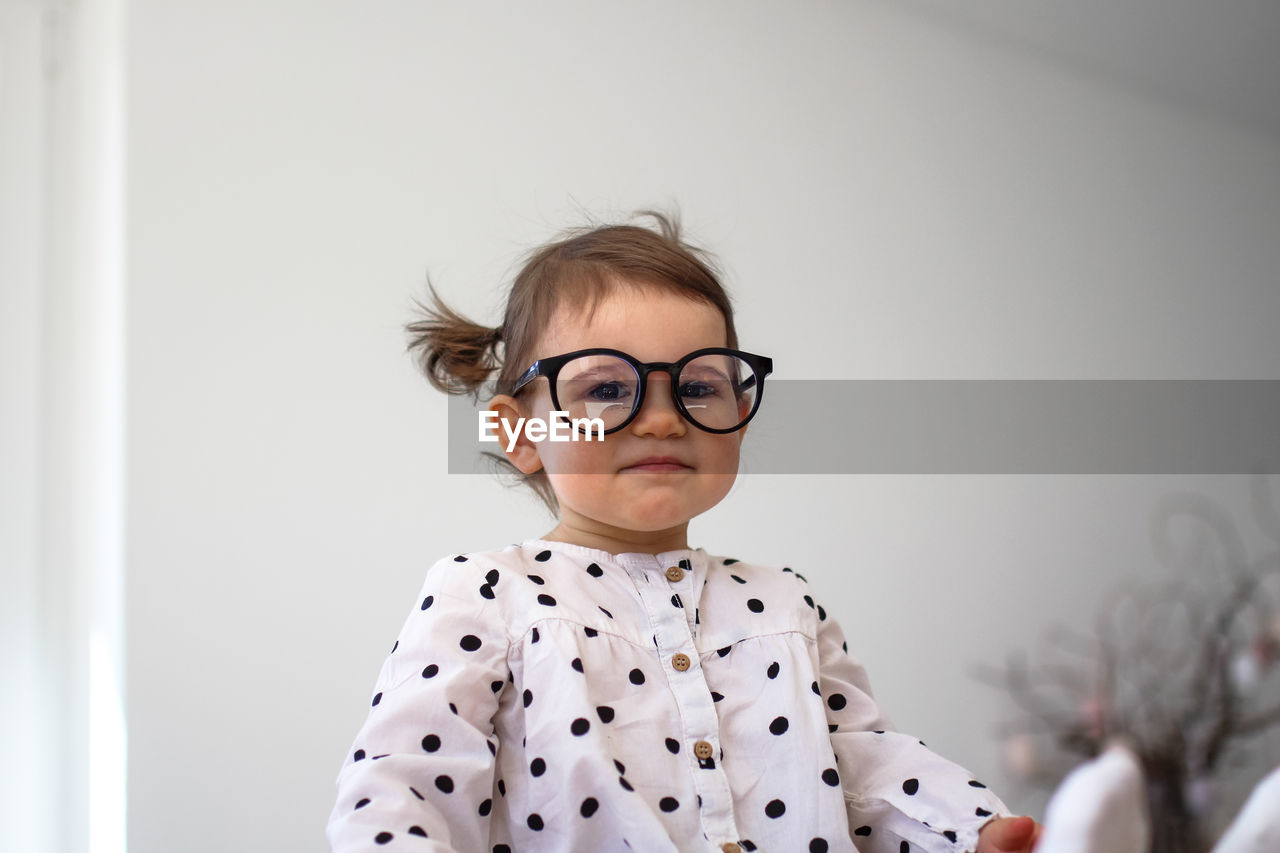 A little girl with glasses sits on a wooden table. funny girl 