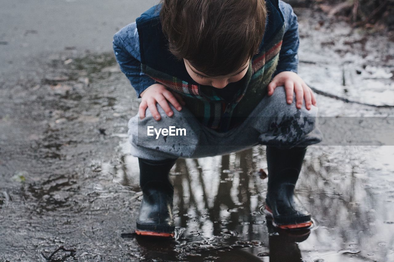 Full length of boy crouching on puddle