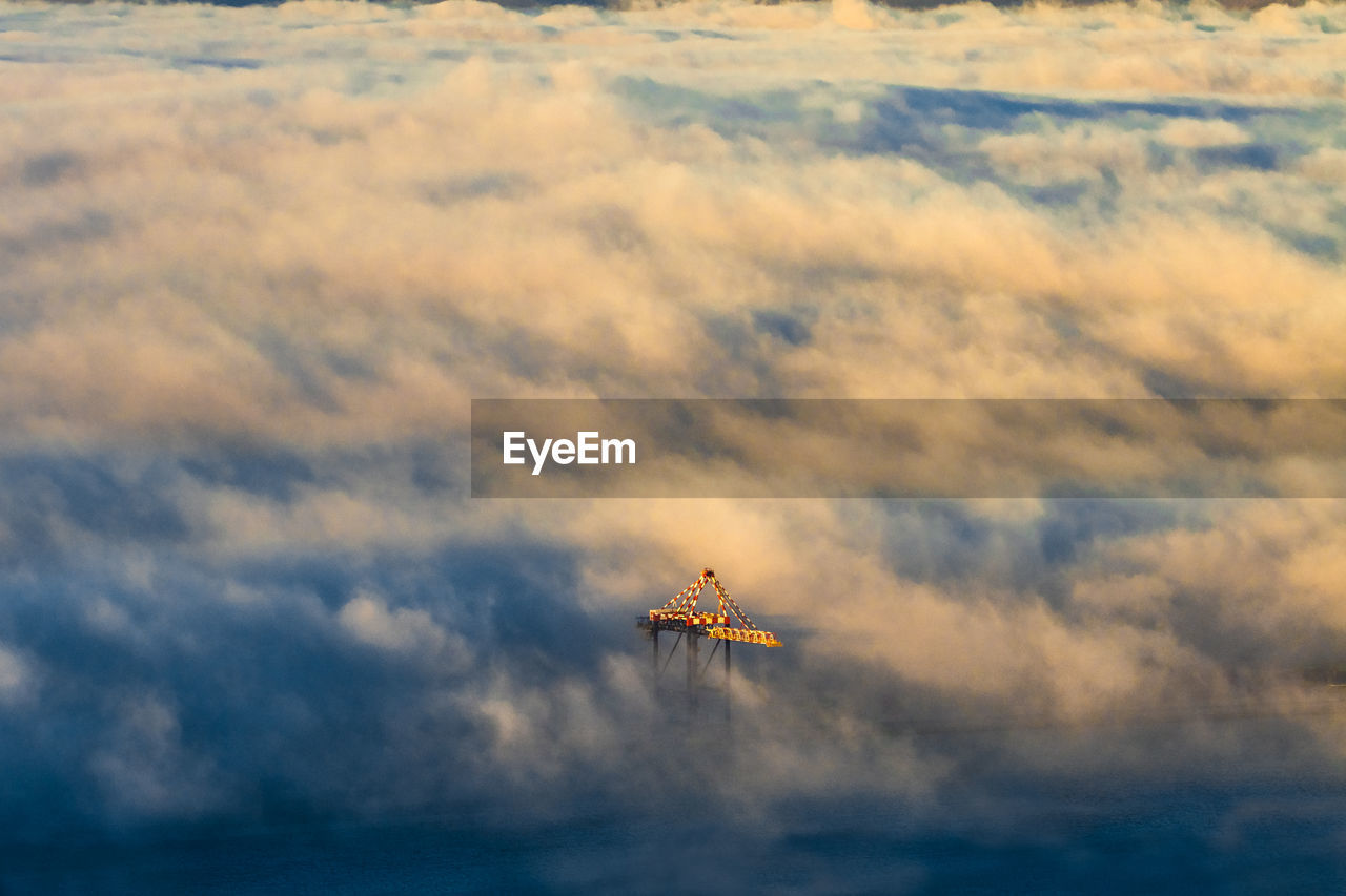 Shipping crane peeking out of clouds at sunset