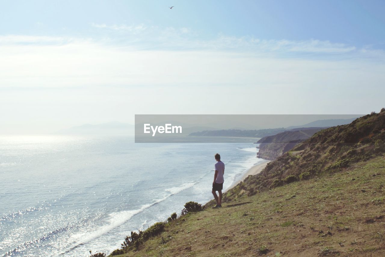 MAN STANDING ON SHORE AGAINST SKY