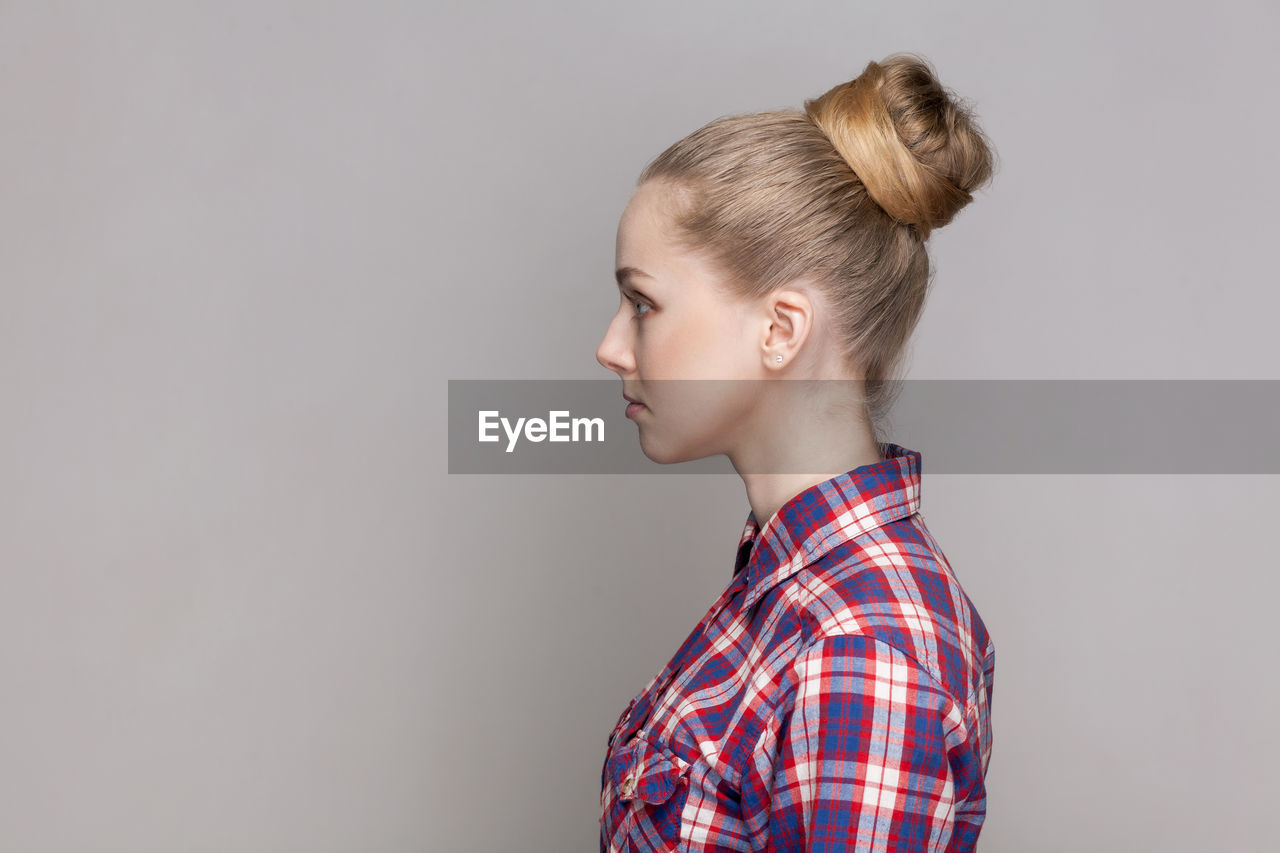 studio shot, childhood, gray background, indoors, child, hairstyle, one person, blond hair, portrait, human hair, gray, copy space, photo shoot, checked pattern, side view, looking, casual clothing, pattern, emotion, bun, cute, profile view, headshot, colored background, women, hair bun, portrait photography, waist up, plaid, clothing, standing, white background, human face, innocence