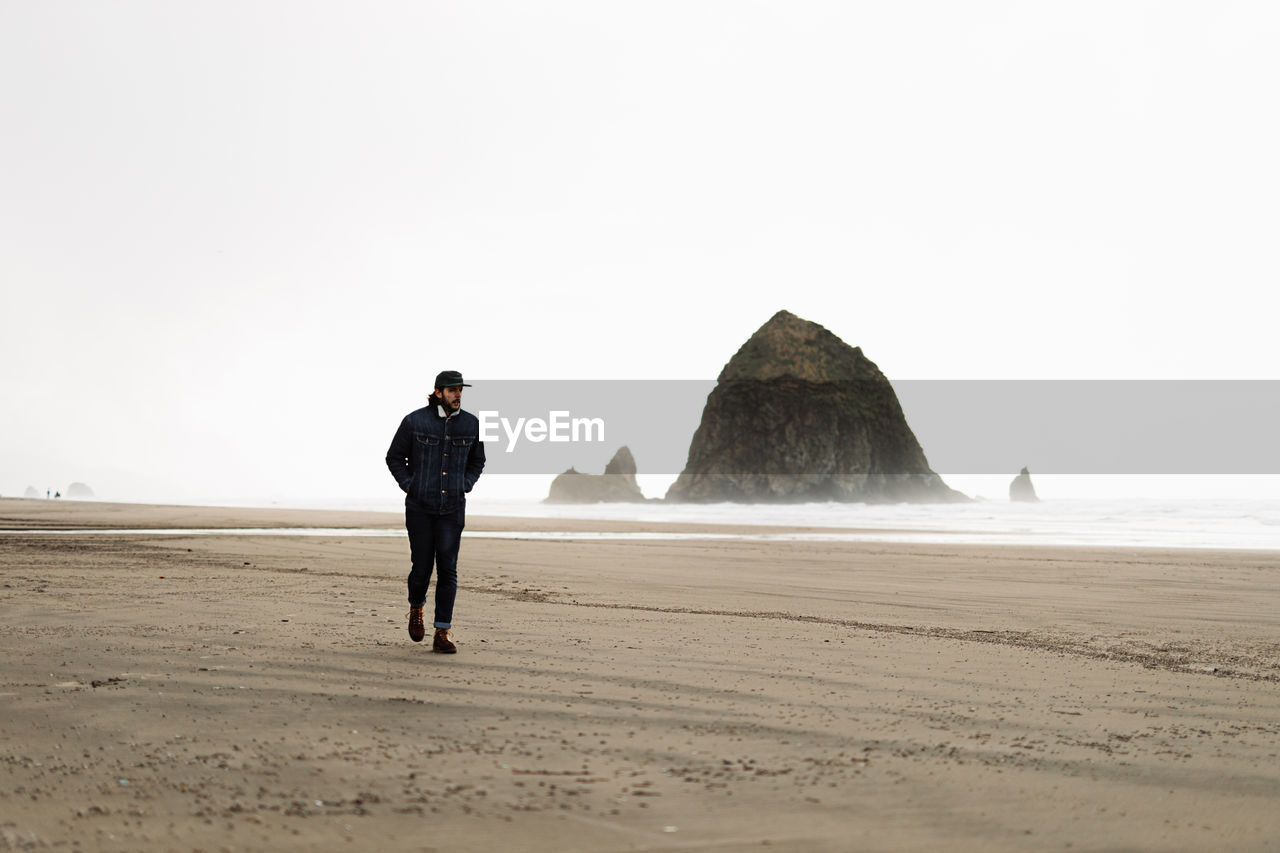 Man traveler walking along foamy beach near sea on overcast day