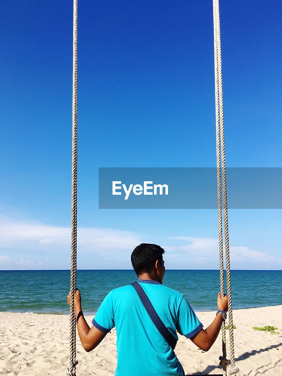 REAR VIEW OF BOY STANDING ON BEACH AGAINST CLEAR BLUE SKY